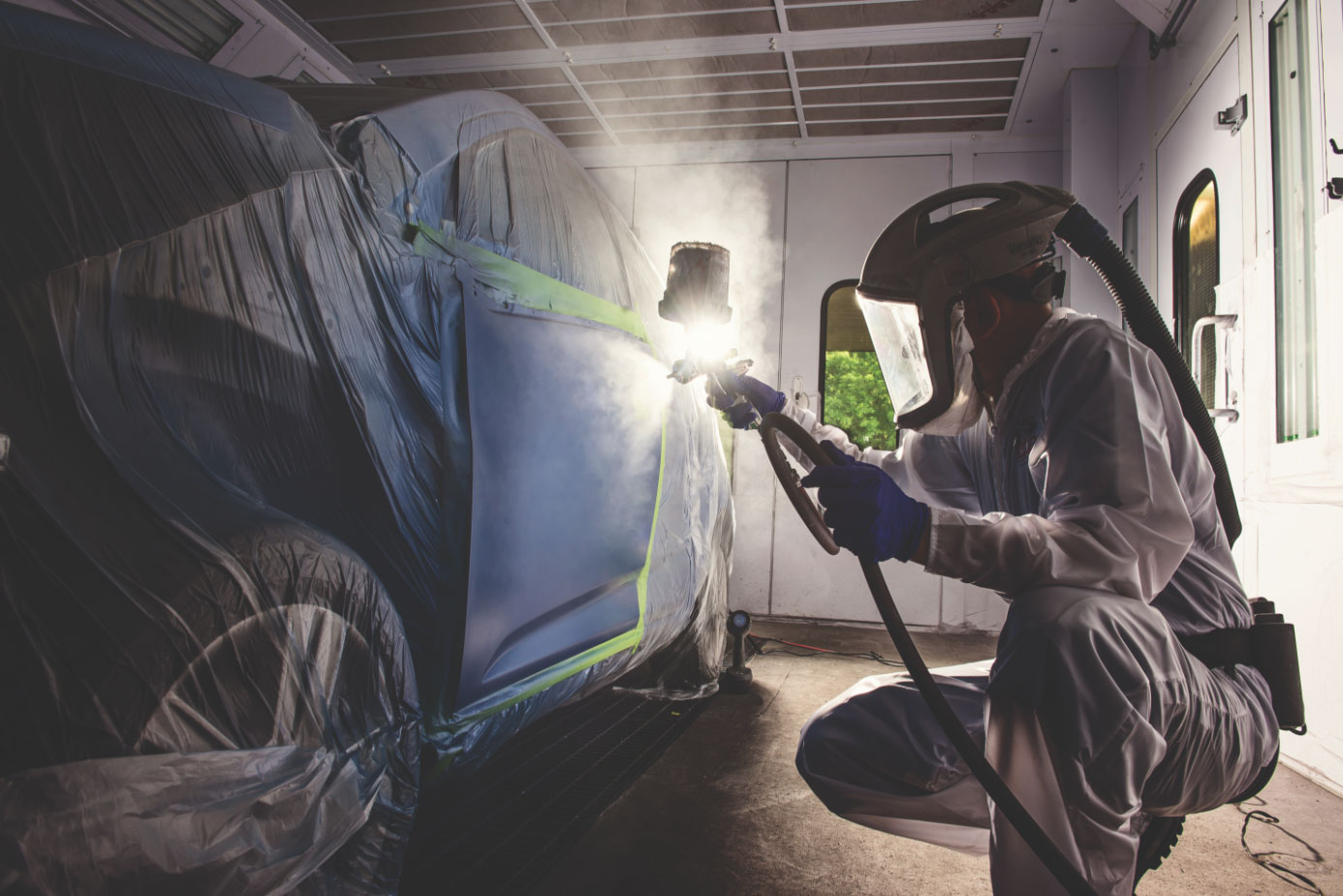 Automobile technican spraying vehicle in paint booth